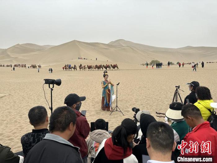 圖為2023年4月底，敦煌大漠“逐舞者”奧楠在鳴沙山月牙泉景區(qū)視頻直播，吸引游人圍觀。　馮志軍 攝